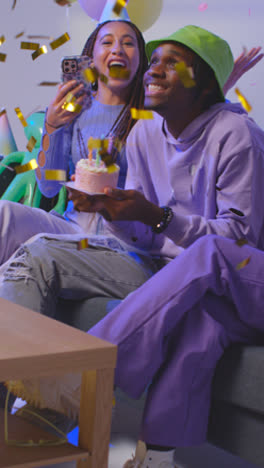 Vertical-Video-Studio-Shot-Of-Gen-Z-Friends-Celebrating-Man's-Birthday-With-Party-Cake-And-Candles-Sitting-On-Sofa